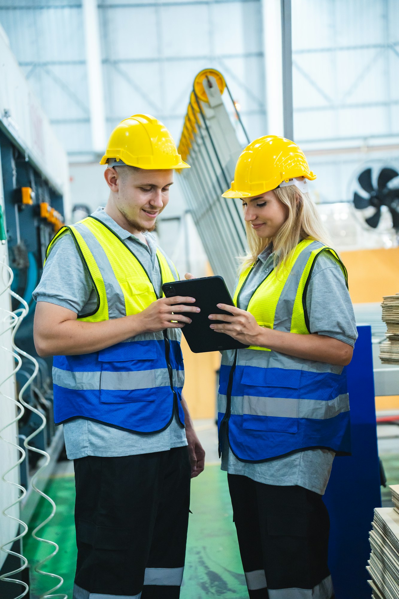 Engineer controlling industrial machine working with assistant worker checking first for labour