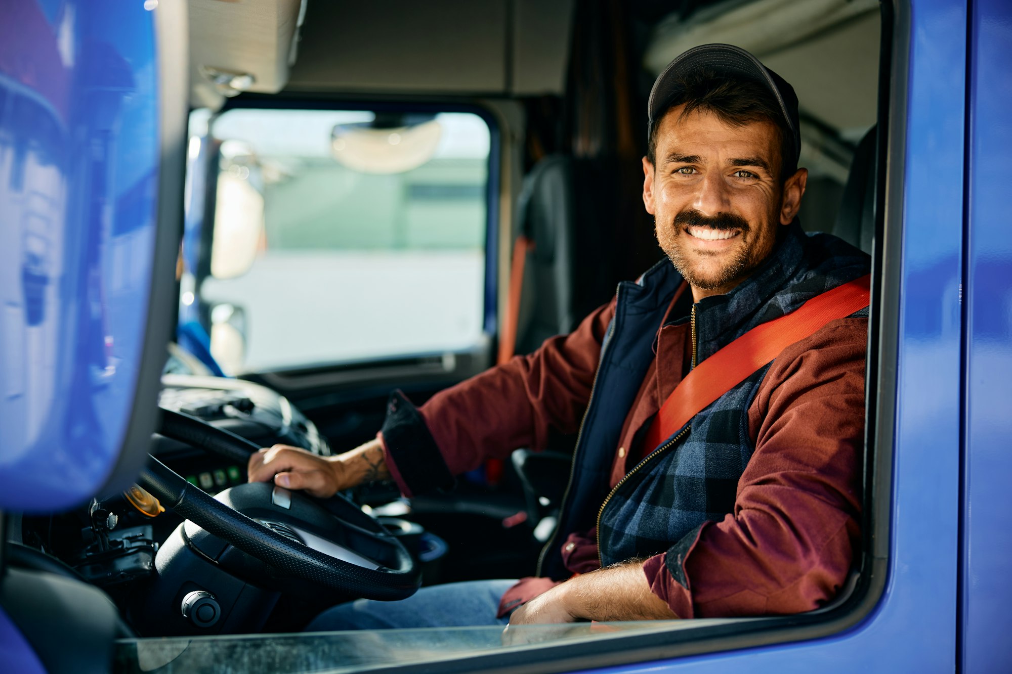 Happy professional truck driver driving his truck and looking at camera.